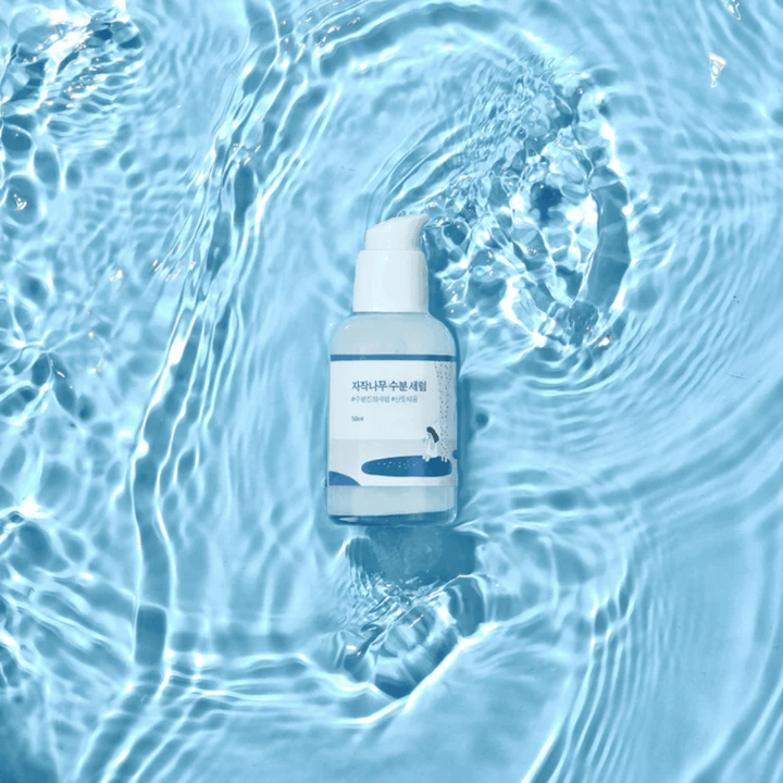 Round Lab Birch Juice Moisturizing Serum i pumpflaska flytande på blått vatten med solljusreflektioner.