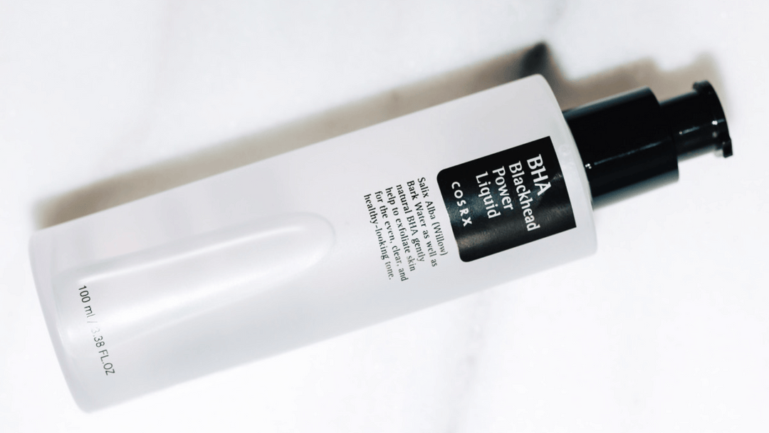 En vit flaska med COSRX BHA Blackhead Power Liquid, liggande på en vit yta med reflektion.