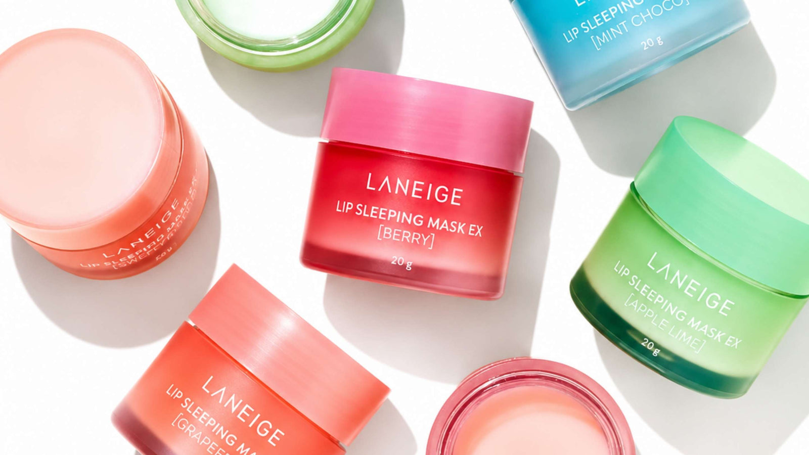 Flera genomskinliga rosa burkar av LANEIGE Lip Sleeping Mask i grapefrukt, spridda på en rosa bakgrund.