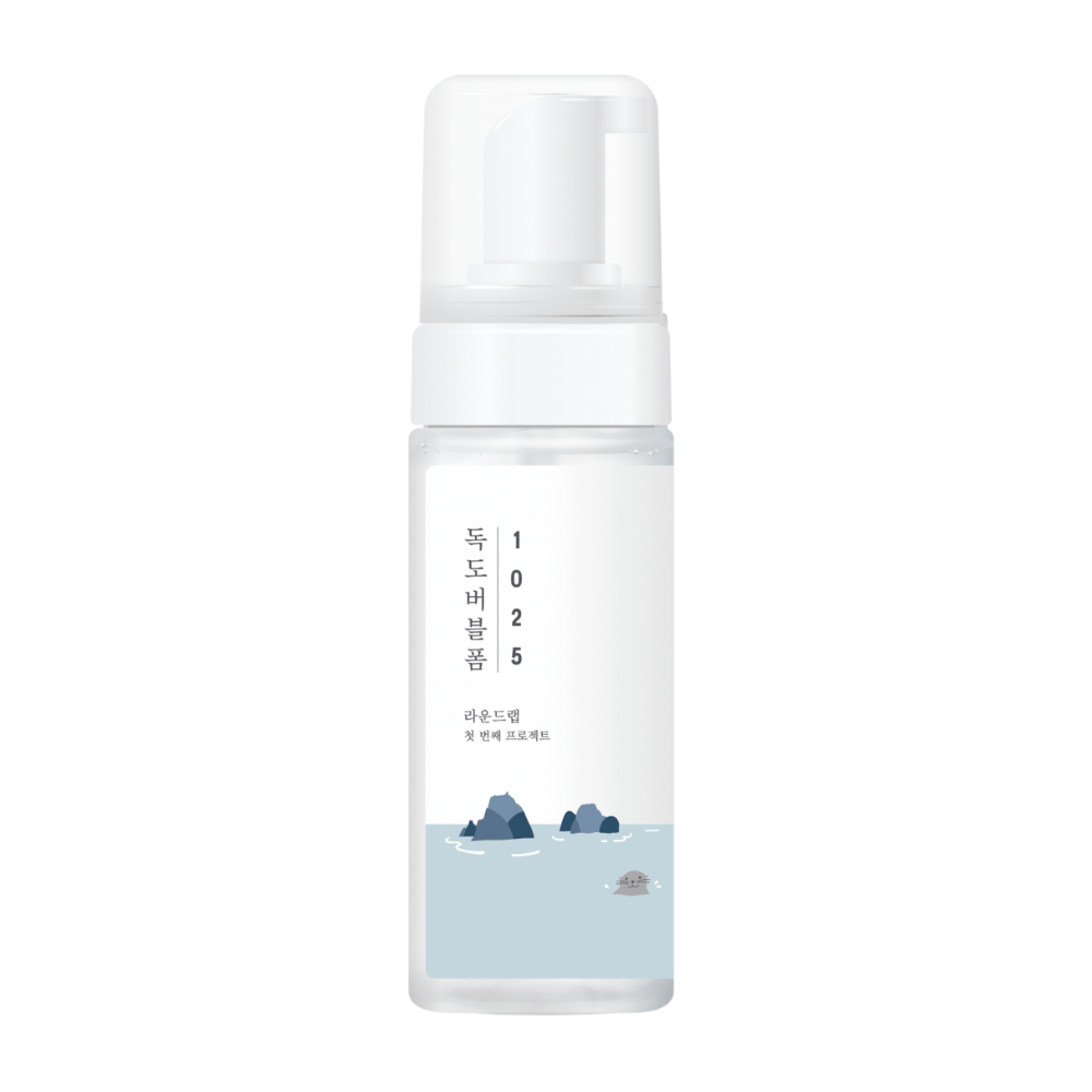 1025 Dokdo Bubble Foam" es un producto de limpieza facial de ROUND LAB, empaquetado en una botella de bomba blanca con un diseño sencillo y limpio, adornado con texto e ilustraciones minimalistas de paisajes marinos. 