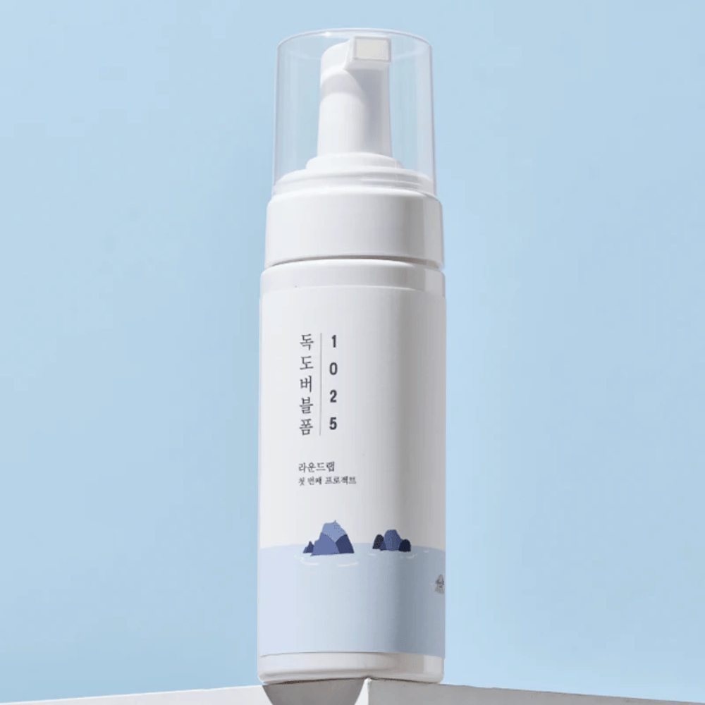  El producto es un "1025 Dokdo Bubble Foam" de ROUND LAB, empaquetado en una botella de bomba blanca con diseño minimalista. Está destinado a la limpieza profunda del rostro sin irritación.