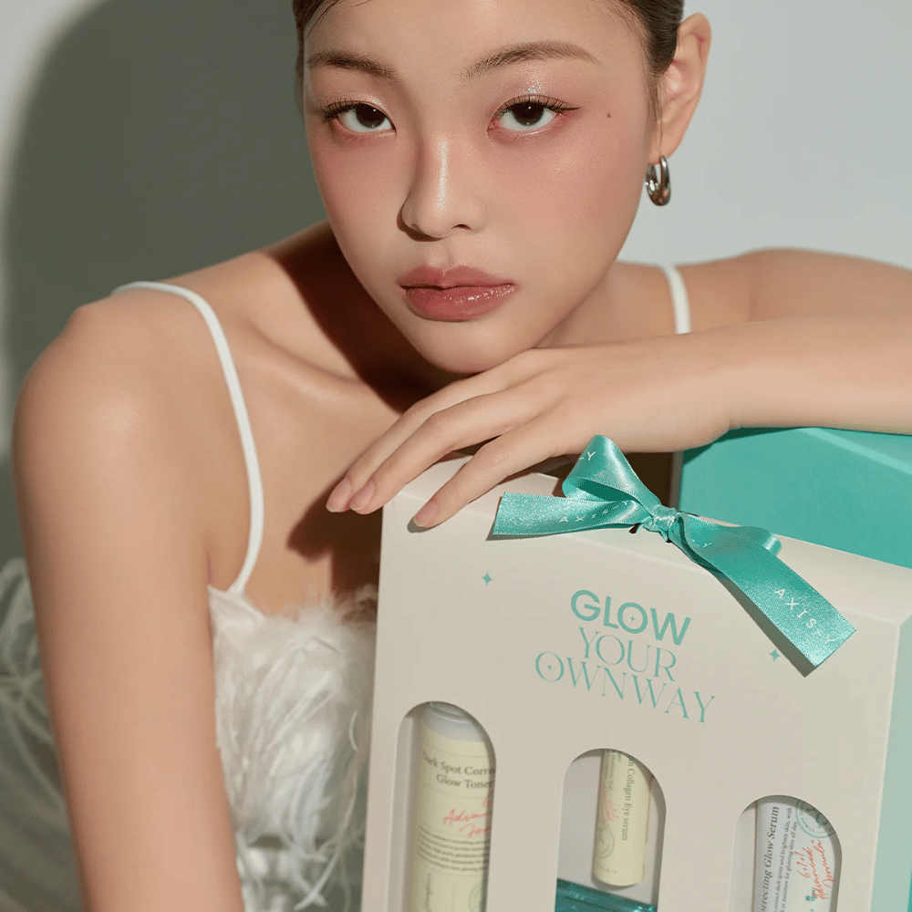 Modelo con maquillaje elegante sostiene la caja de regalo “Glow Your Own Way” de AXIS-Y – un Kit de cuidado de la piel con estilo, perfecto como regalo para ti mismo o para alguien que amas.
