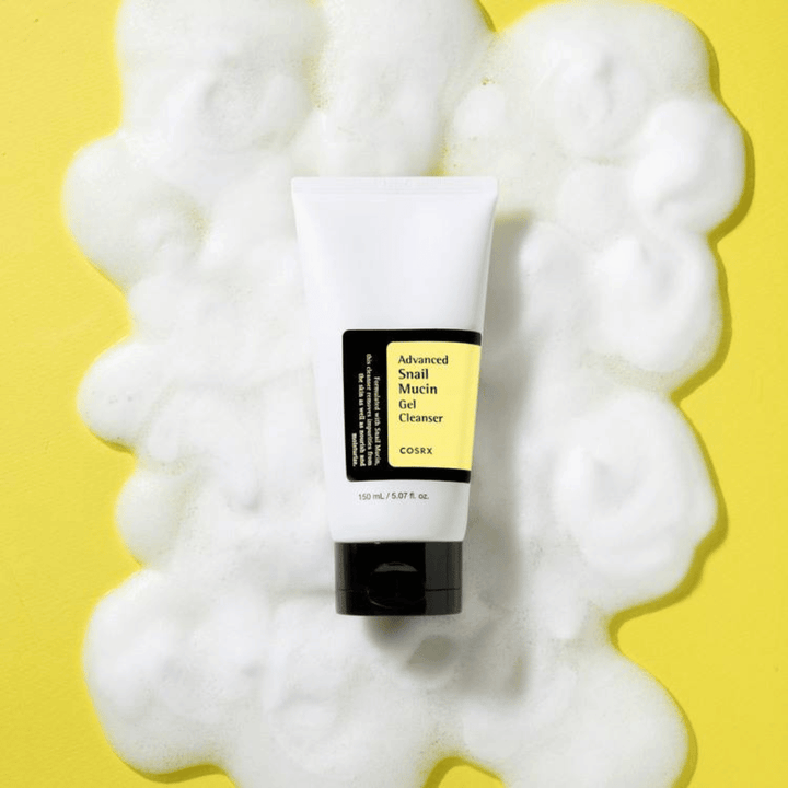COSRX Advanced Snail Mucin Gel Cleanser 150 ml rodeado de abundante espuma sobre fondo amarillo – limpieza facial coreana suave con snail mucin para hidratación y brillo.