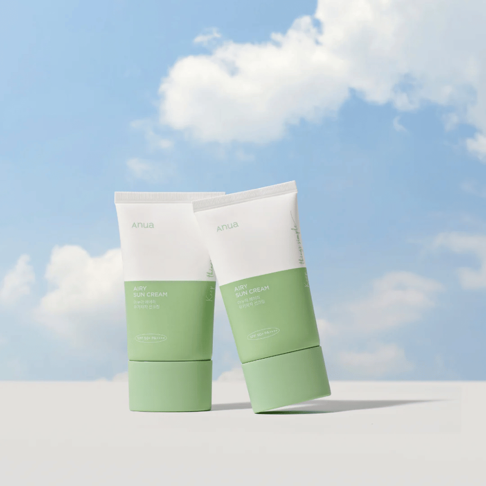 Dos tubos de Anua Airy Sun Cream contra un cielo con nubes blancas.