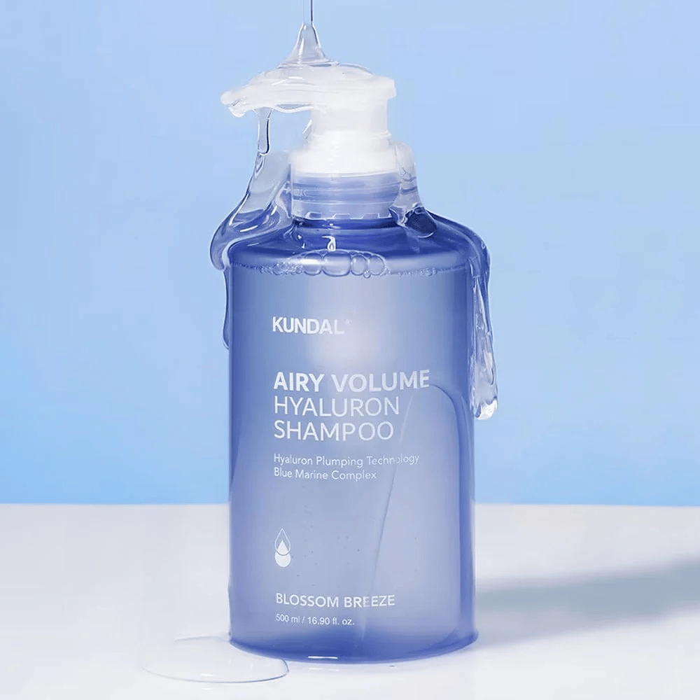 KUNDAL Airy Volume Hyaluron Shampoo Blossom Breeze en botella de bomba azul, con ácido hialurónico y Blue Marine Complex, fotografiado con agua corriente.