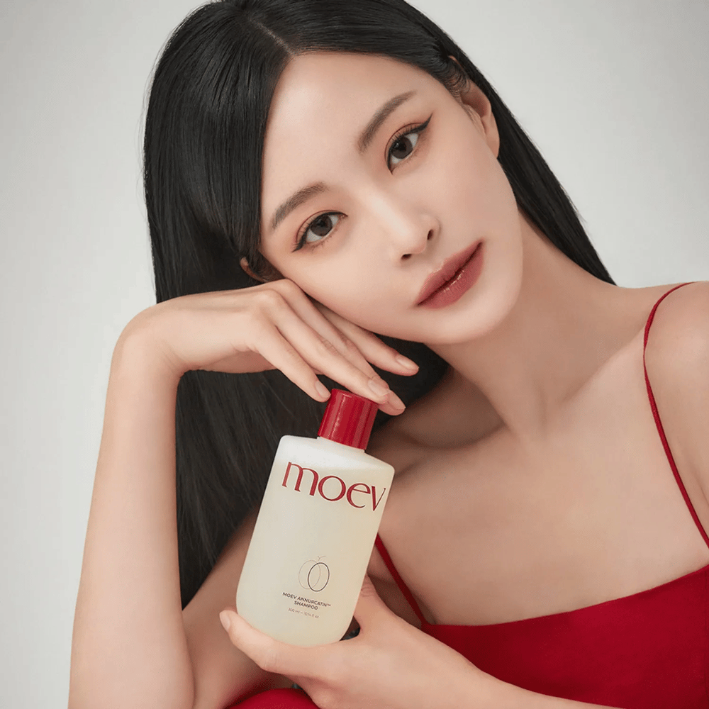 Mujer con cabello largo y brillante sostiene MOEV Annurcatin Shampoo – un champú coreano que hidrata, fortalece y protege el cabello con ingredientes naturales.