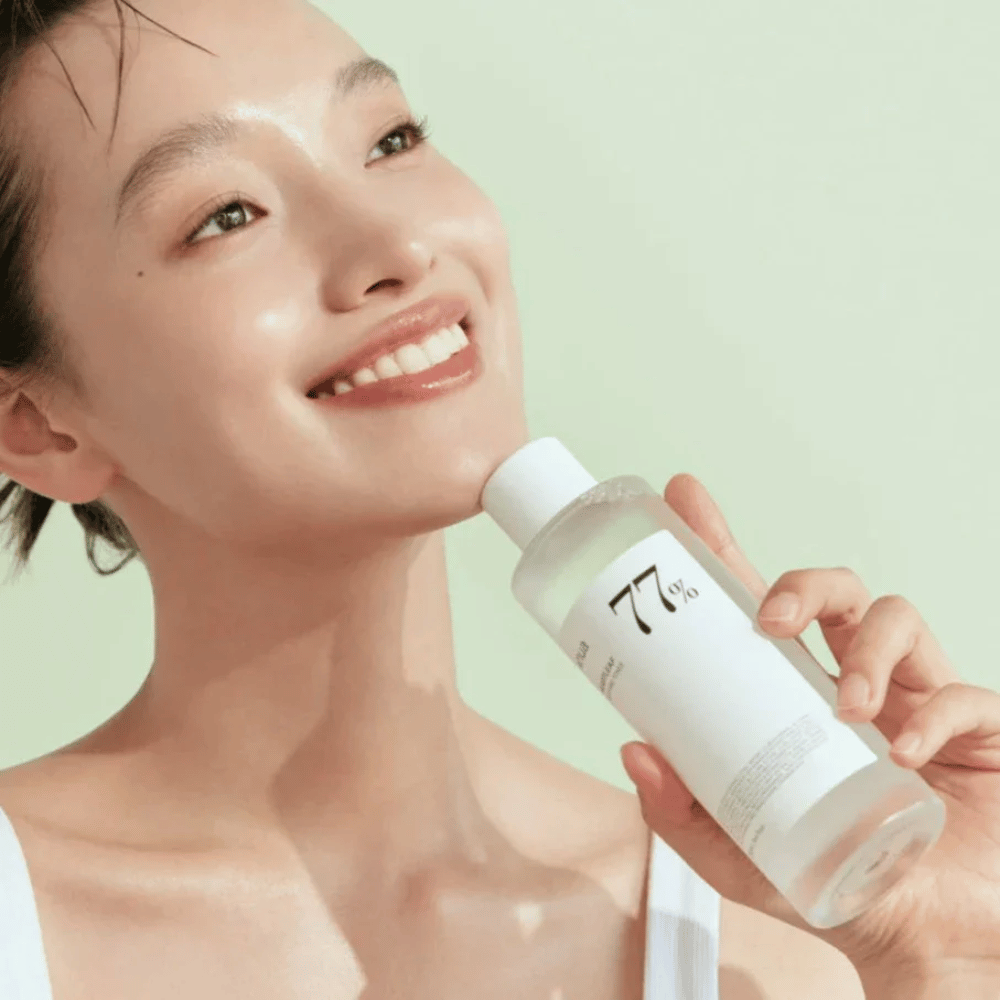 Una mujer calma su piel sensible con una botella Heartleaf 77% Soothing Toner de Anua, que contiene extracto de hoja de camaleón.