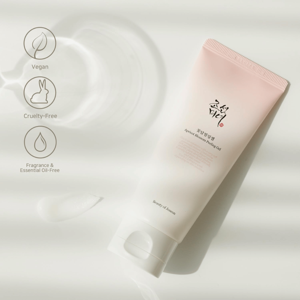 Un tubo con Apricot Blossom Peeling Gel se encuentra sobre una superficie reflectante con iconos que indican que el producto es vegano, amigable con los animales y libre de fragancias y aceites esenciales.