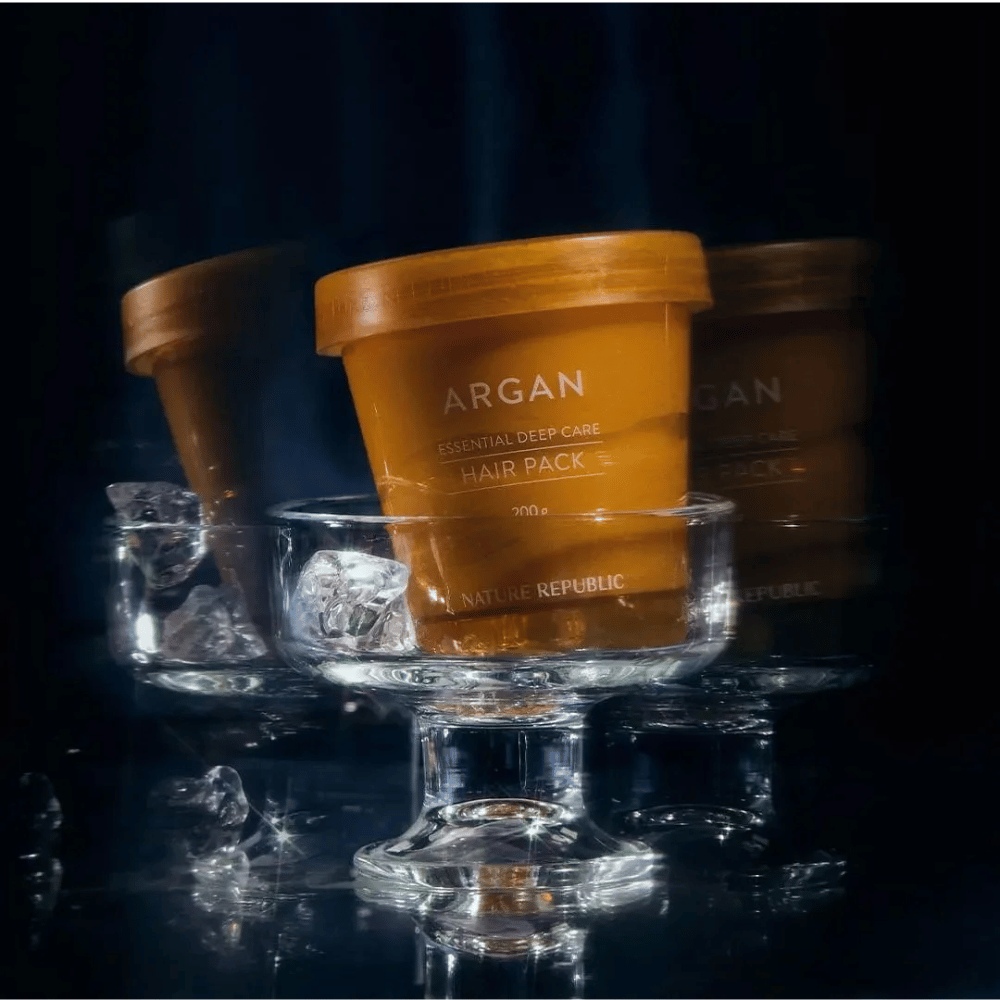 Nature Republic Argan Essential Moisture Repairing Hair Mask colocada en un plato de vidrio con cubitos de hielo – mascarilla capilar lujosa y nutritiva.