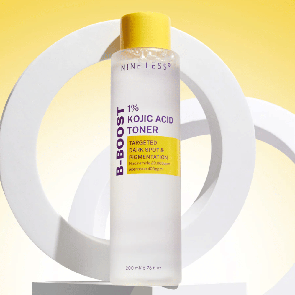 NINE LESS B-Boost 1% Kojic Acid Toner de pie contra un fondo amarillo con el texto "Targeted Dark Spot & Pigmentation". Tónico igualador del tono de piel con niacinamida y adenosina.