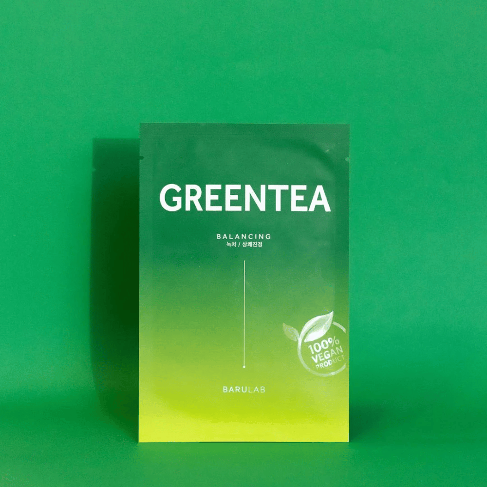 Un paquete de BARULAB para una máscara "GREENTEA Balancing", marcado como "100% Vegan Product". El color del paquete pasa de verde oscuro en la parte superior a un verde más claro en la parte inferior, sobre un fondo verde uniforme.