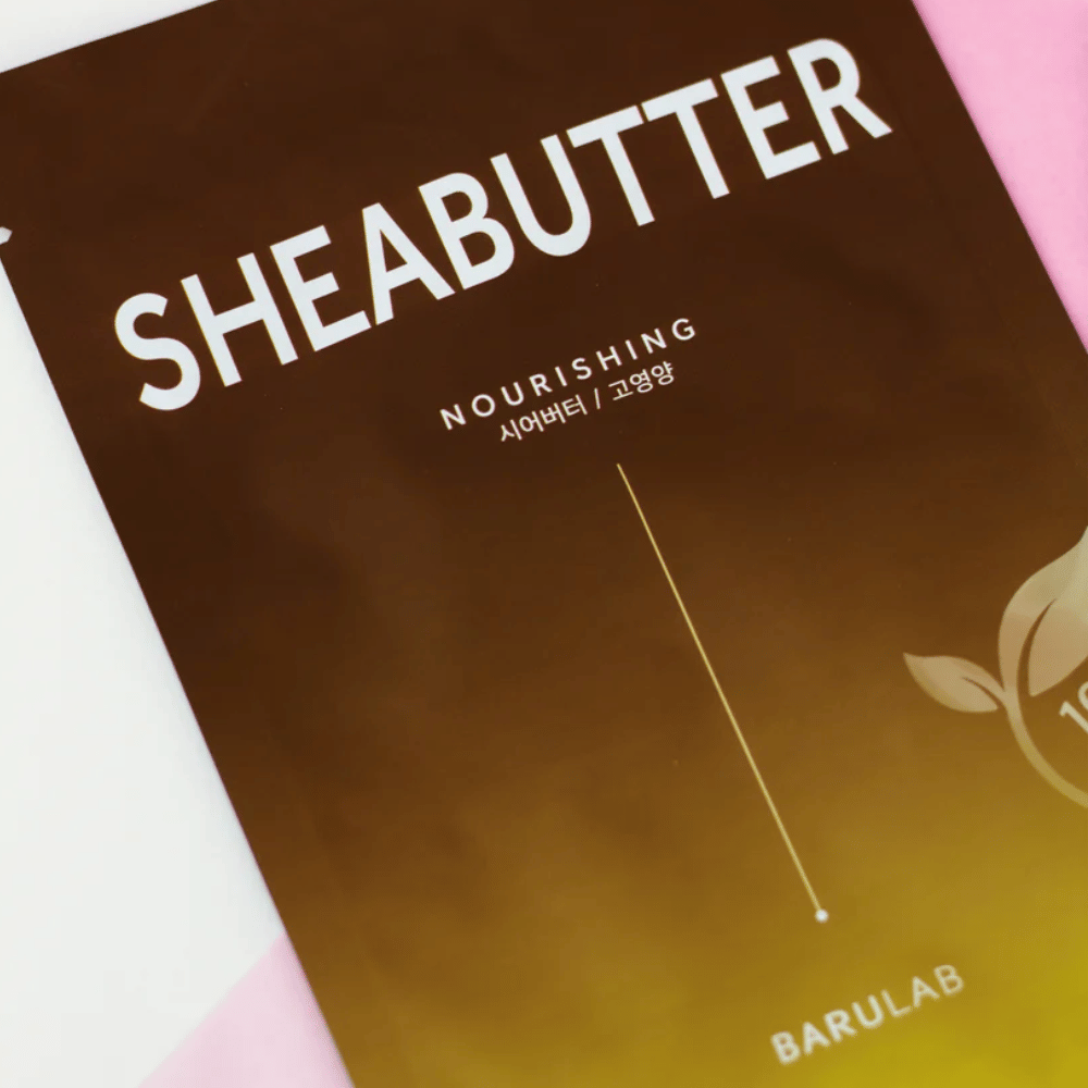 Un primer plano de un paquete de la máscara "SHEABUTTER Nourishing" BARULAB. El producto está etiquetado como "100% Vegan Product" y tiene un degradado de color de marrón oscuro a marrón claro.