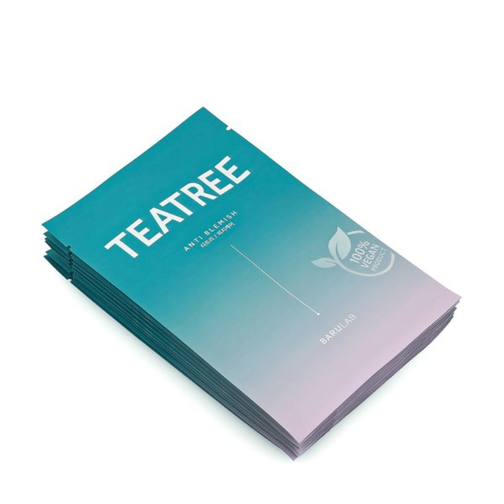 Una pila de paquetes de BARULAB máscaras "TEATREE Anti Blemish", todas etiquetadas como "Producto 100% Vegano". Los paquetes tienen un color turquesa uniforme.