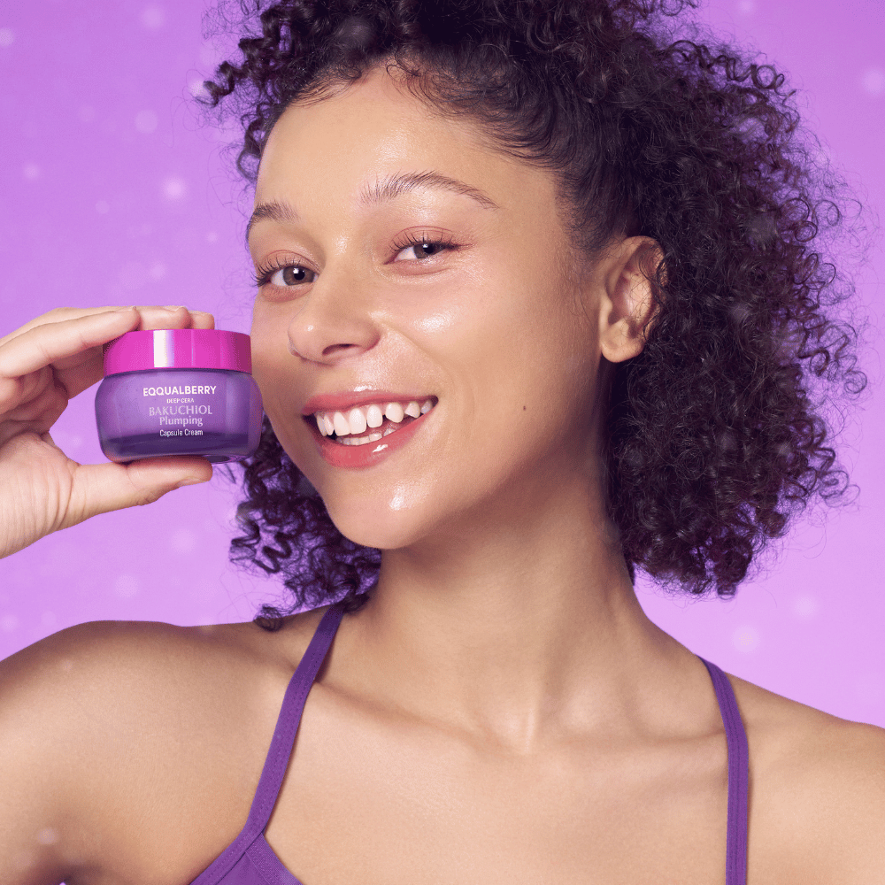 Mujer con piel radiante sostiene EQQUALBERRY Bakuchiol Plumping Capsule Cream y sonríe frente a un fondo morado.