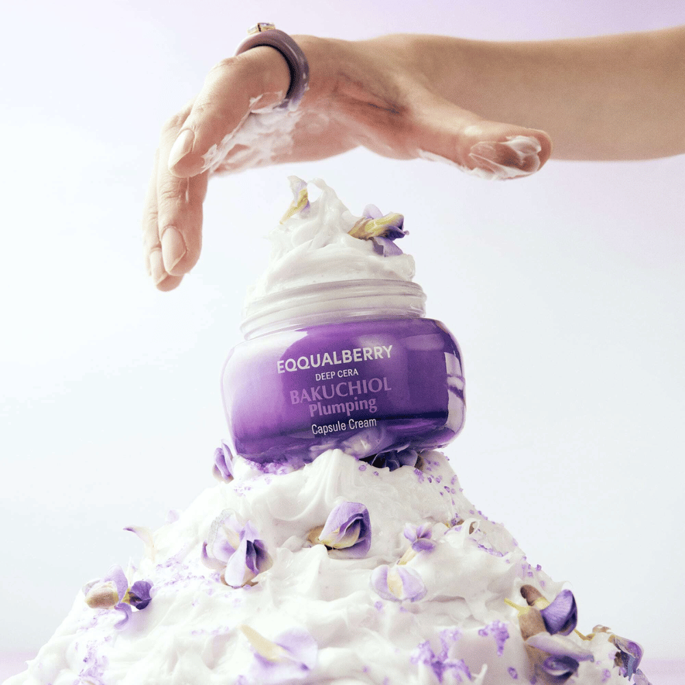 EQQUALBERRY Bakuchiol Plumping Capsule Cream colocado sobre una pila de crema batida con pétalos de flores – simboliza humedad y cuidado.