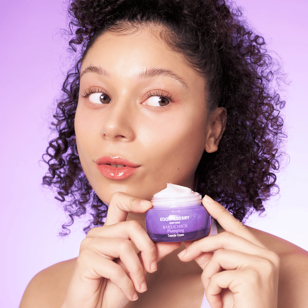 Mujer sostiene EQQUALBERRY Bakuchiol Plumping Capsule Cream en la mano y muestra su piel hidratada y luminosa contra un fondo morado.