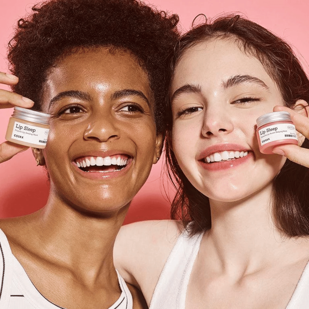 Dos personas sonríen y sostienen frascos de COSRX Lip Sleep. La imagen transmite labios suaves, hidratados y el efecto natural de resplandor del producto.