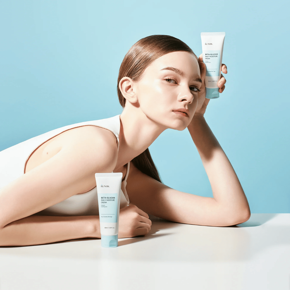 Imagen de estilo de vida en la que una modelo posa con iUNIK Beta-Glucan Daily Moisture Cream sobre un fondo azul claro. La imagen transmite una sensación limpia, fresca e hidratante, al mismo tiempo que el producto se muestra claramente.