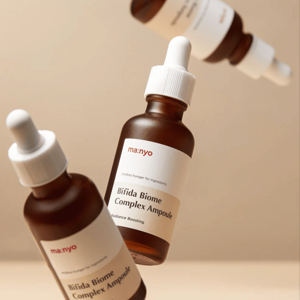Imagen de producto con varias botellas flotantes de ma:nyo Bifida Biome Complex Ampoule sobre fondo beige que aporta una sensación moderna y minimalista.