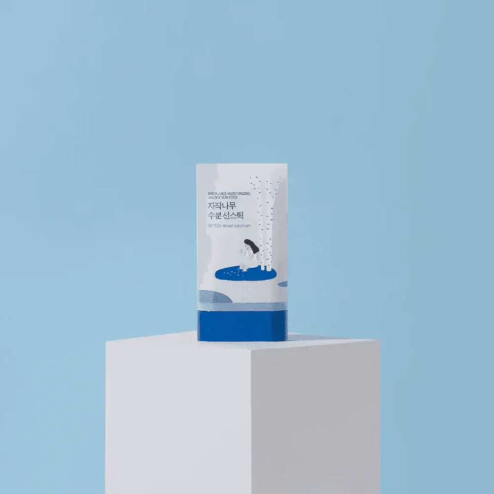 ROUND LAB Birch Juice Moisturizing Sun Stick SPF50+ está sobre un pedestal contra un fondo azul: protección solar hidratante en formato stick