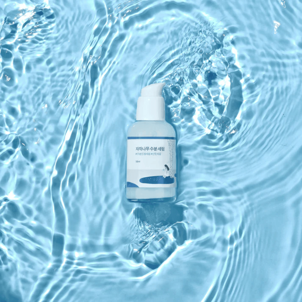 Round Lab Birch Juice Moisturizing Serum en botella de bomba flotando en agua azul con reflejos de luz solar.