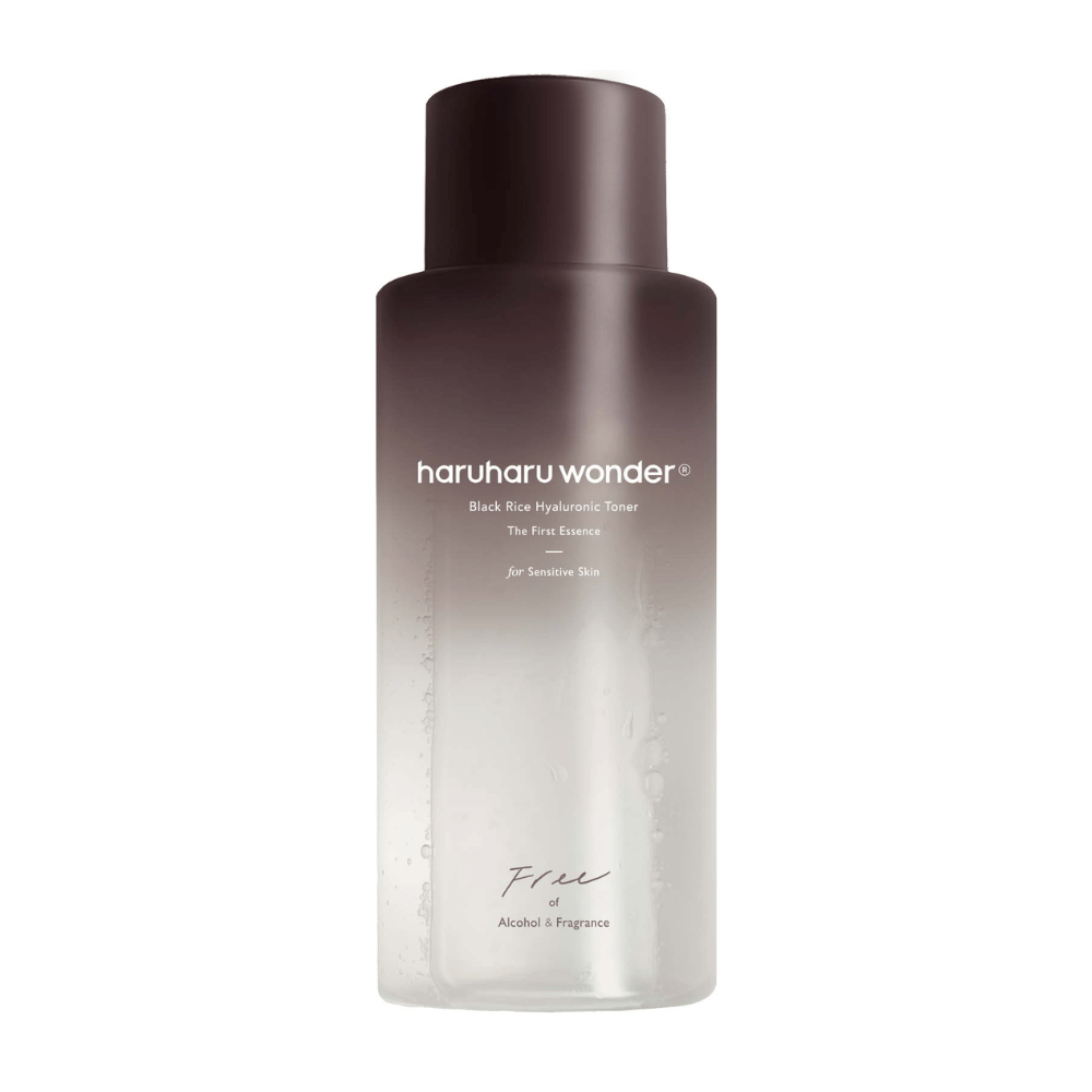 Una botella de haruharu wonder Black Rice Hyaluronic Toner The First Essence, con un degradado de marrón oscuro a transparente y el texto "Libre de Alcohol y Fragancia", sobre fondo blanco.