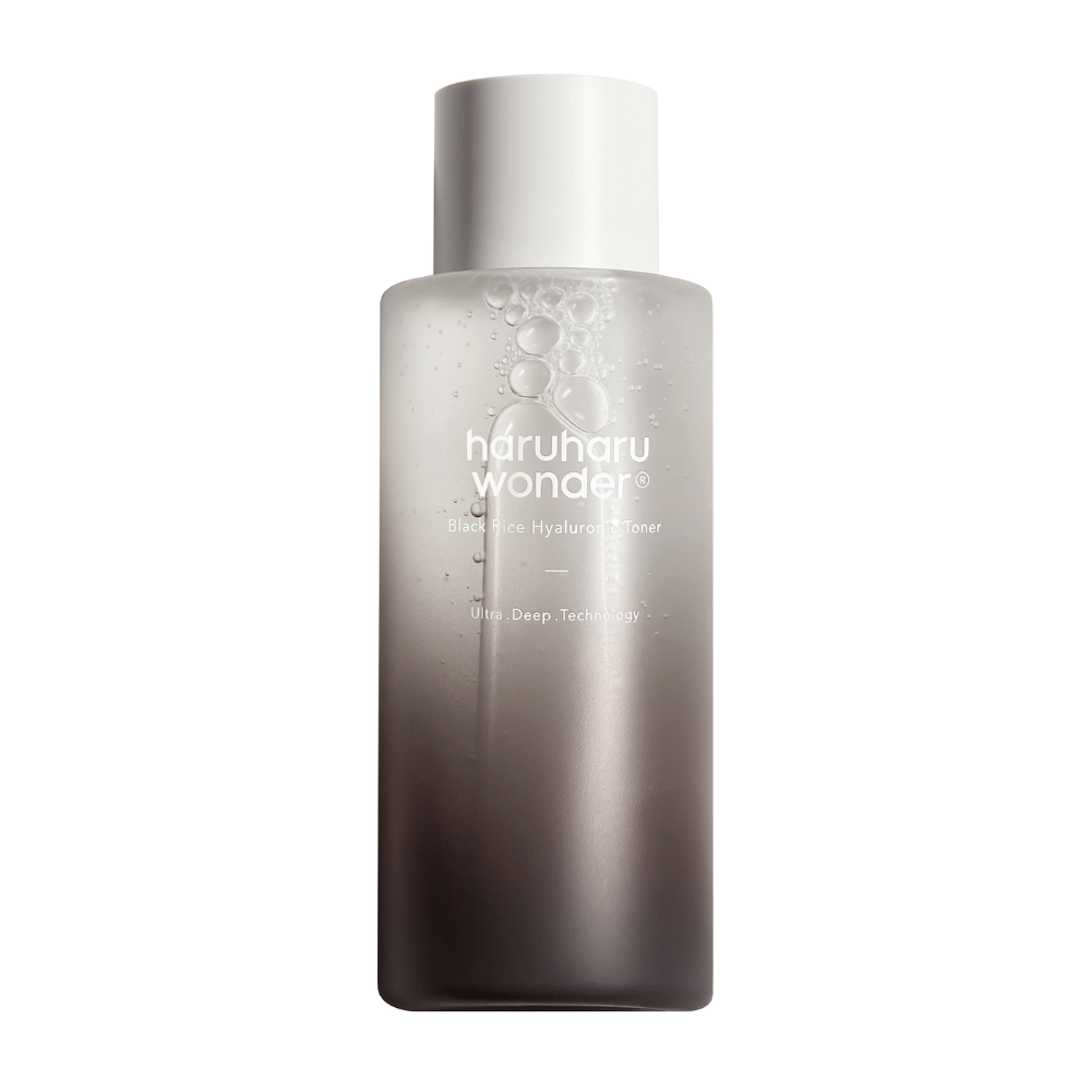 Una botella de haruharu wonder Black Rice Hyaluronic Toner con un degradado de color de gris a blanco y gotas de agua en la superficie, sobre un fondo blanco.