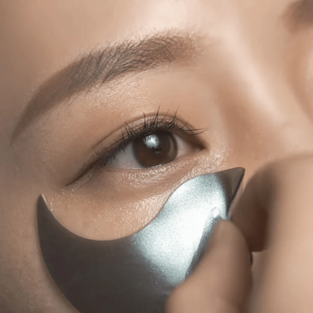 Imagen detallada en la que se aplica un parches para ojos de hidrogel negro debajo del ojo. La imagen muestra el ajuste ceñido y la sensación refrescante alrededor del área de los ojos.