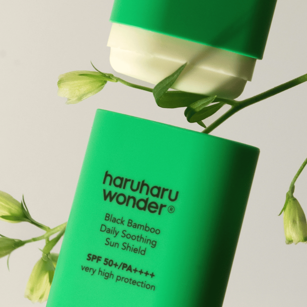 Primer plano de Haruharu Wonder Black Bamboo Daily Soothing Sun Shield – un protector solar verde en formato de barra con SPF 50+ PA++++, rodeado de detalles de plantas verdes.