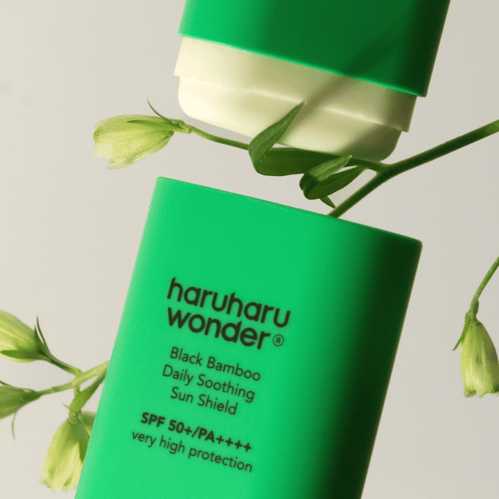 Närbild av Haruharu Wonder Black Bamboo Daily Soothing Sun Shield – ett grönt solskydd i stiftformat med SPF 50+ PA++++, omgiven av gröna växtdetaljer.