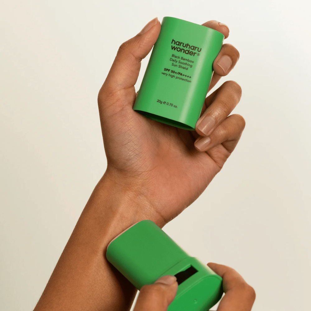 En person applicerar Haruharu Wonder Black Bamboo Daily Soothing Sun Shield – en grön solskyddsstick med SPF 50+ PA++++ – på handleden.