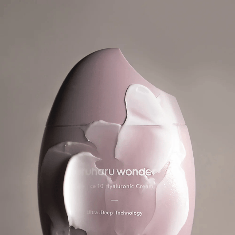 La imagen muestra un frasco de "Haruharu Wonder Black Rice 10 Hyaluronic Cream", que está parcialmente cubierto por una crema espesa y transparente. El texto en la imagen sugiere el uso de tecnología avanzada para la hidratación profunda de la piel. El diseño es moderno y minimalista.