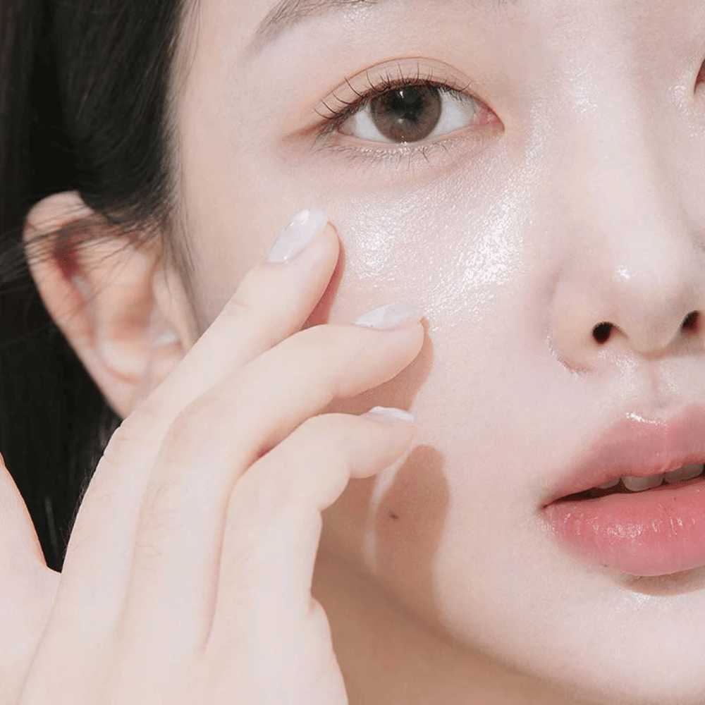 Primer plano de una mujer aplicando crema de ojos debajo del ojo con las yemas de los dedos. La piel se ve hidratada, brillante y cuidada con un resplandor natural.