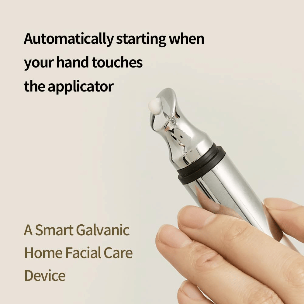 Primer plano de una mano sosteniendo un aplicador galvánico para crema de ojos con función de inicio automático al tacto. El texto en la imagen describe la función y el dispositivo como una herramienta inteligente para el cuidado facial en el hogar.