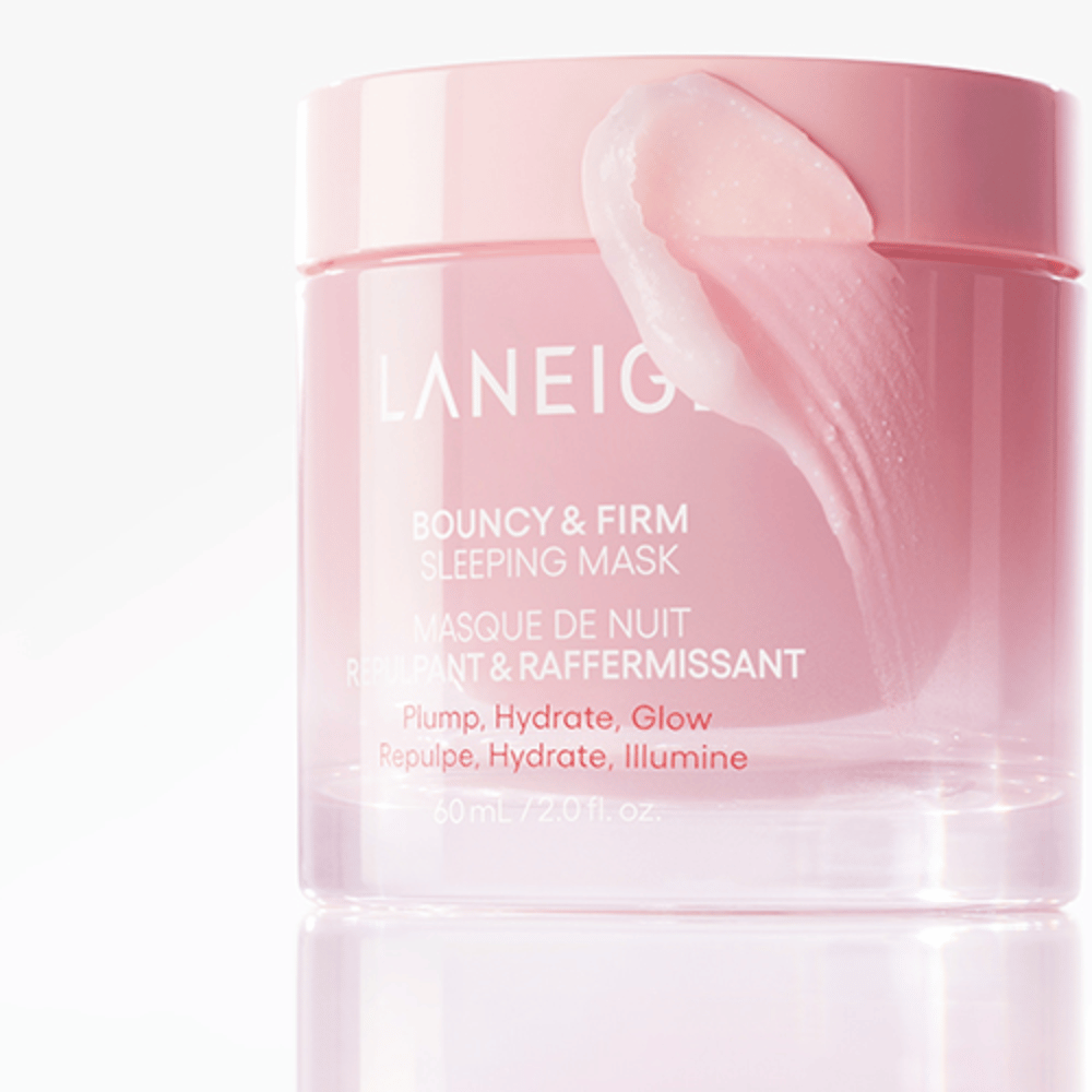 Primer plano de Laneige Bouncy & Firm Sleeping Mask en un tarro rosa, con parte de la mascarilla aplicada en el borde de la tapa. El producto está destinado a proporcionar volumen, hidratación y brillo. El tarro contiene 60 ml y tiene el texto "Volumen, Hidratación, Brillo."