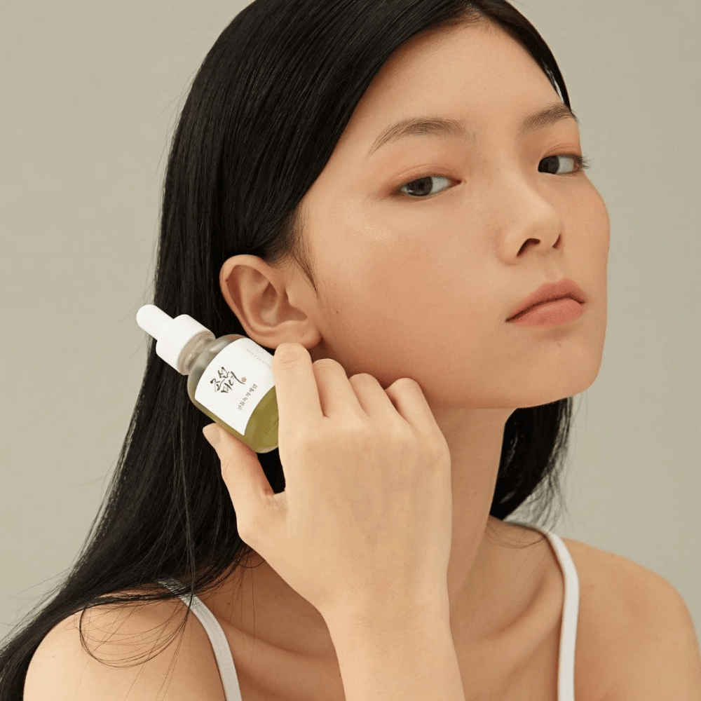 Modelo sostiene Beauty of Joseon Calming Serum en la mejilla – té verde y pantenol que fortalece la barrera de la piel.