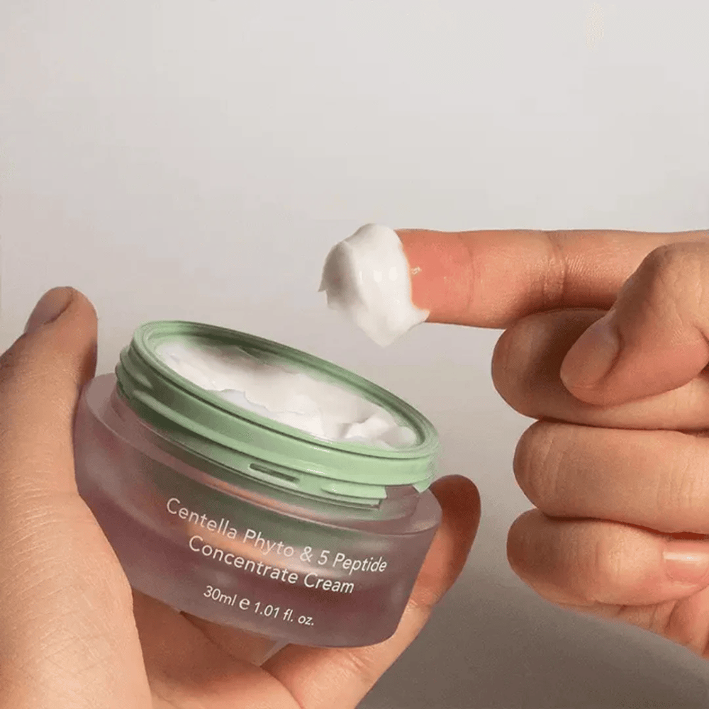 Mano tomando un poco de Centella Phyto & 5 Peptide Concentrate Cream de un tarro.