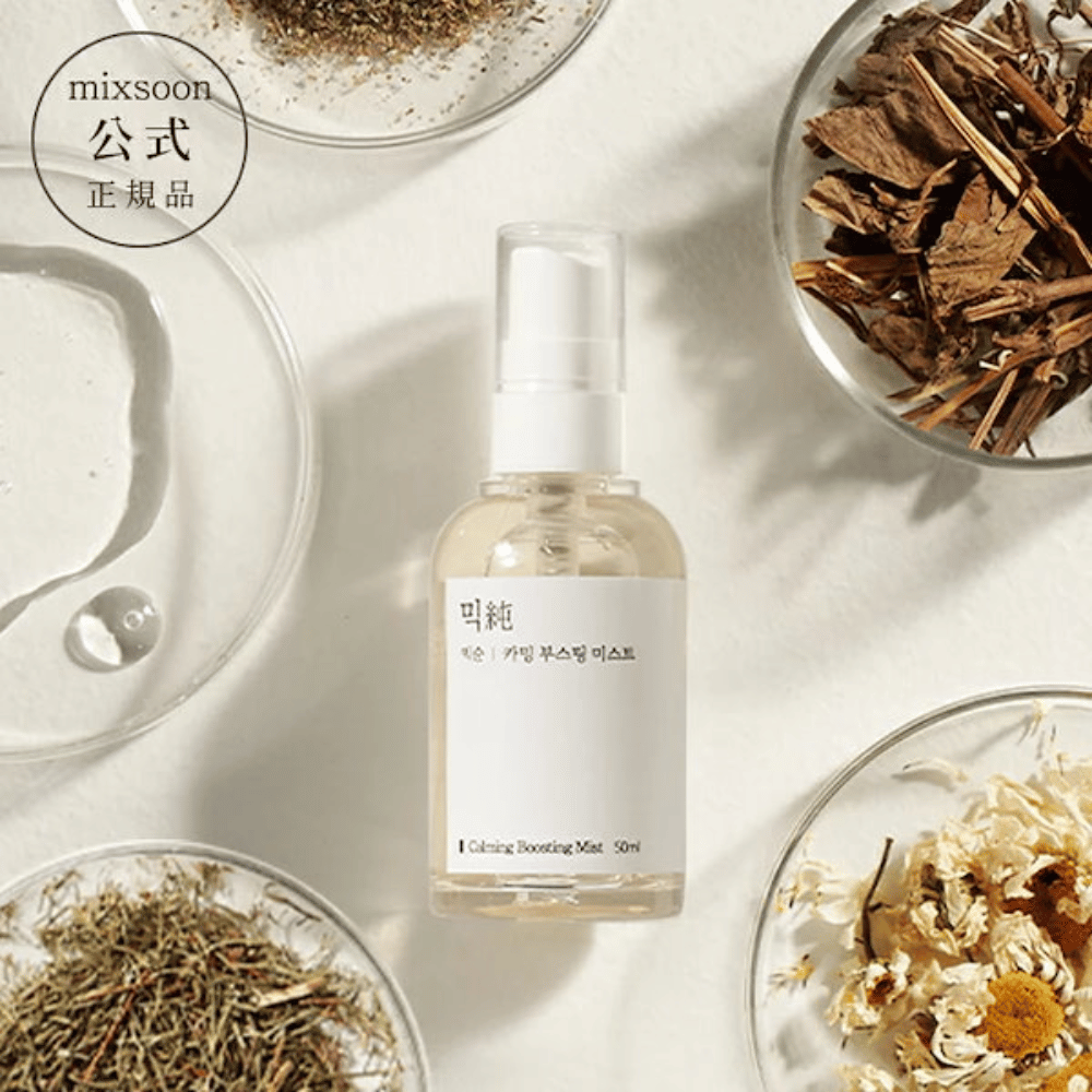 Una botella de spray transparente con la etiqueta 'Calming Boosting Mist' de Mixsoon, rodeada de hierbas secas y flores en cuencos blancos sobre un fondo beige, lo que resalta los ingredientes naturales de los productos.