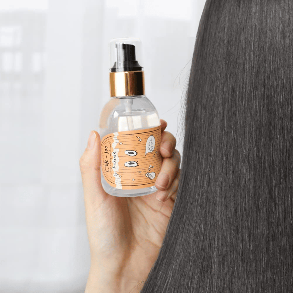 Una persona sostiene CER-100 Hair Essence junto a un cabello largo y brillante para mostrar suavidad y cuidado.
