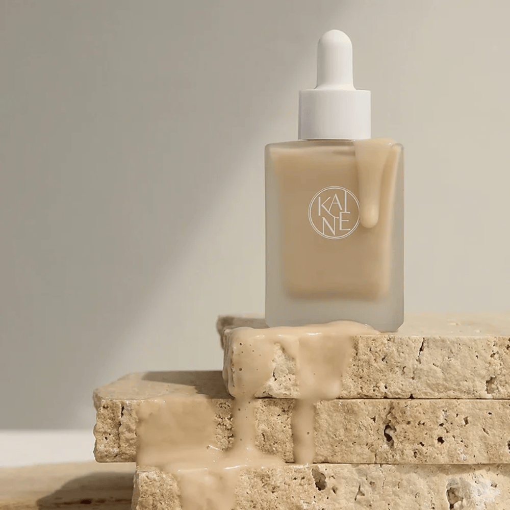 KANE Chaga Collagen Charging Serum en una botella de vidrio esmerilado con pipeta. Textura cremosa fluye sobre piedras naturales en una luz suave y minimalista.