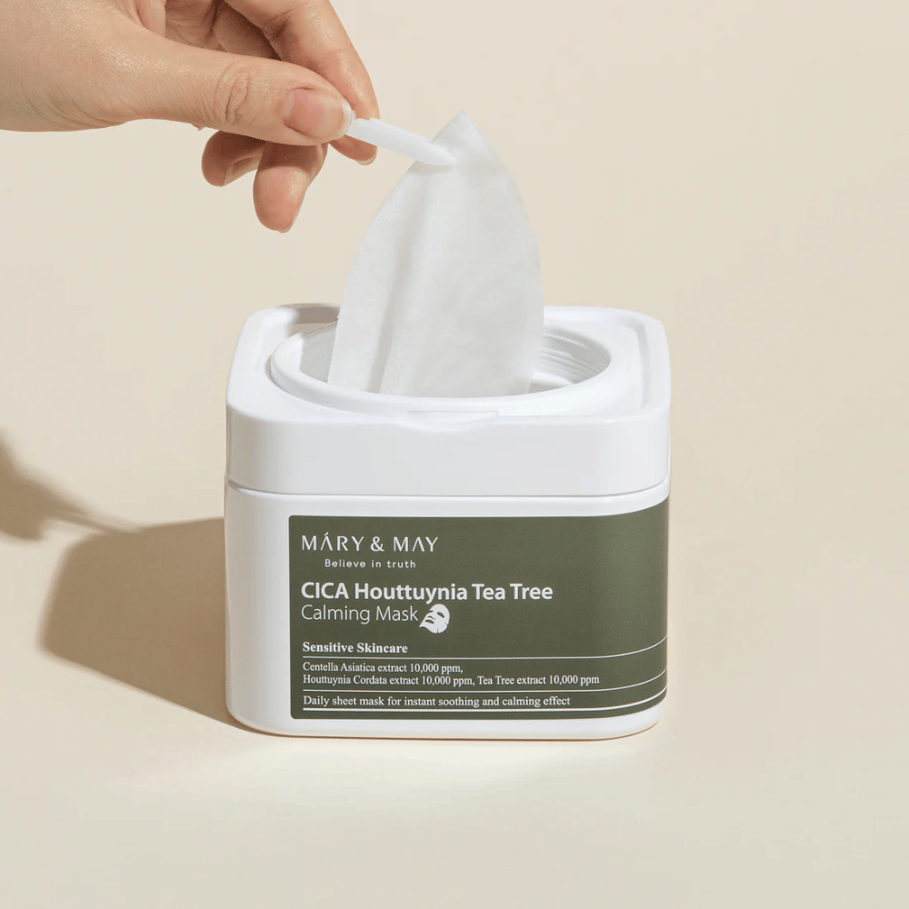 Mano sacando una mascarilla de la tarro Mary & May Cica Houttuynia Tea Tree Calming Mask – mascarilla facial calmante para piel sensible con Cica y extracto de Tea Tree.