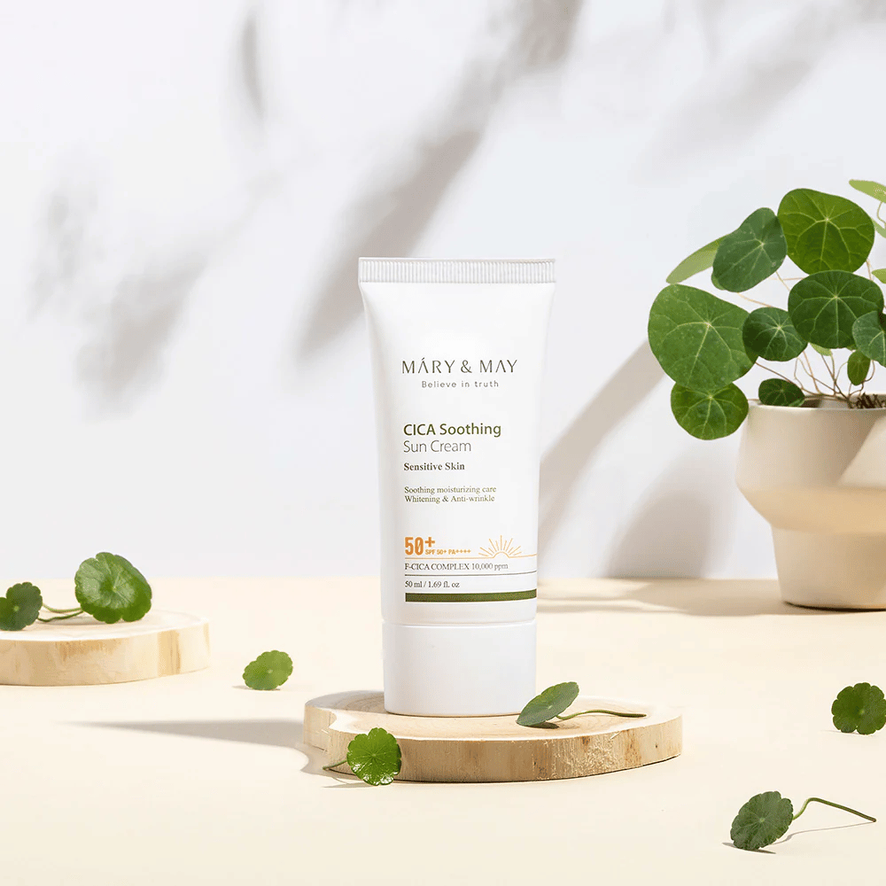 Mary&May CICA Soothing Sun Cream colocada sobre un podio de madera con hojas verdes de centella alrededor. La imagen enfatiza los ingredientes calmantes para la piel y la inspiración natural detrás del producto.