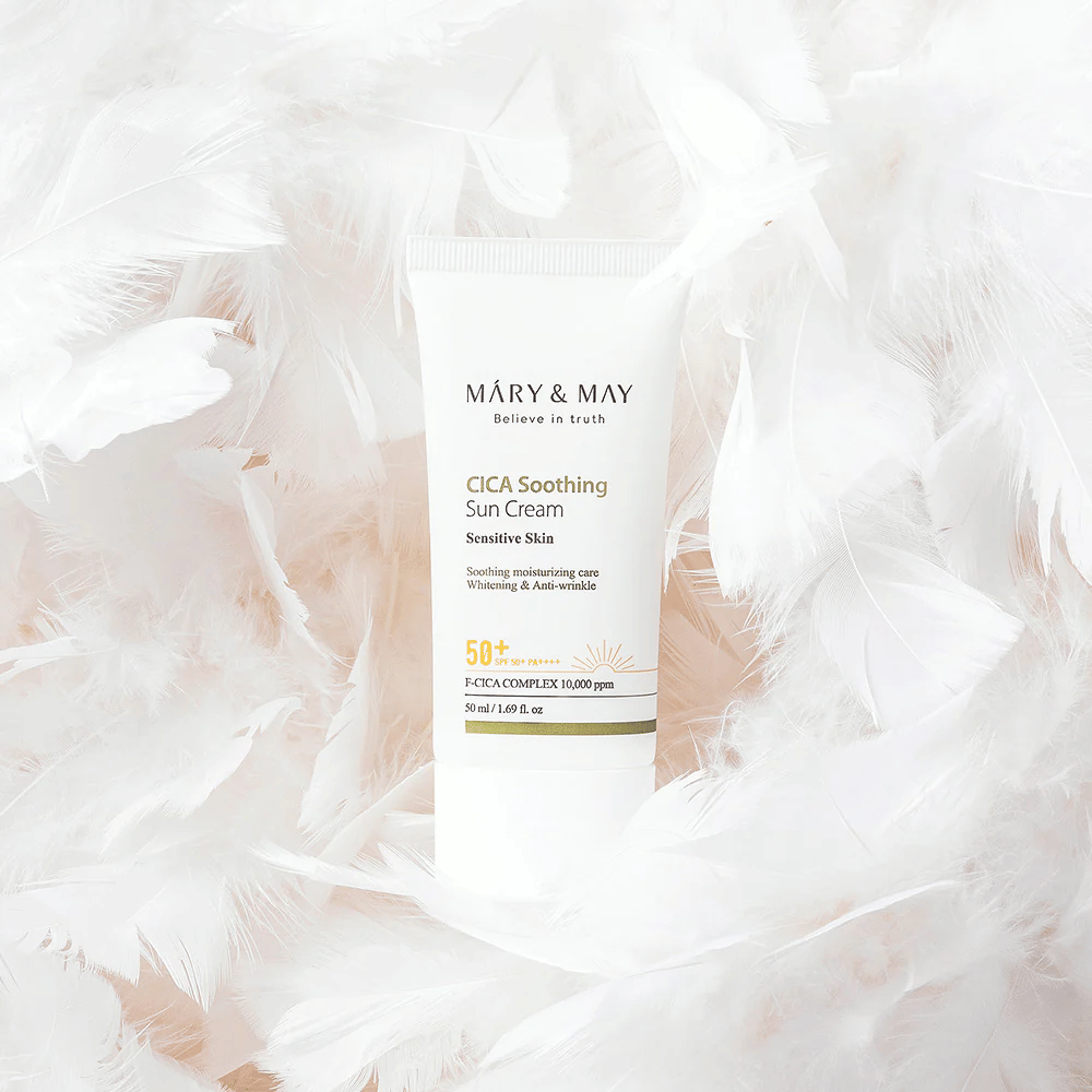Mary&May CICA Soothing Sun Cream rodeada de suaves plumas blancas. La imagen transmite una sensación de suavidad, comodidad y una fórmula ligera adaptada para piel sensible.