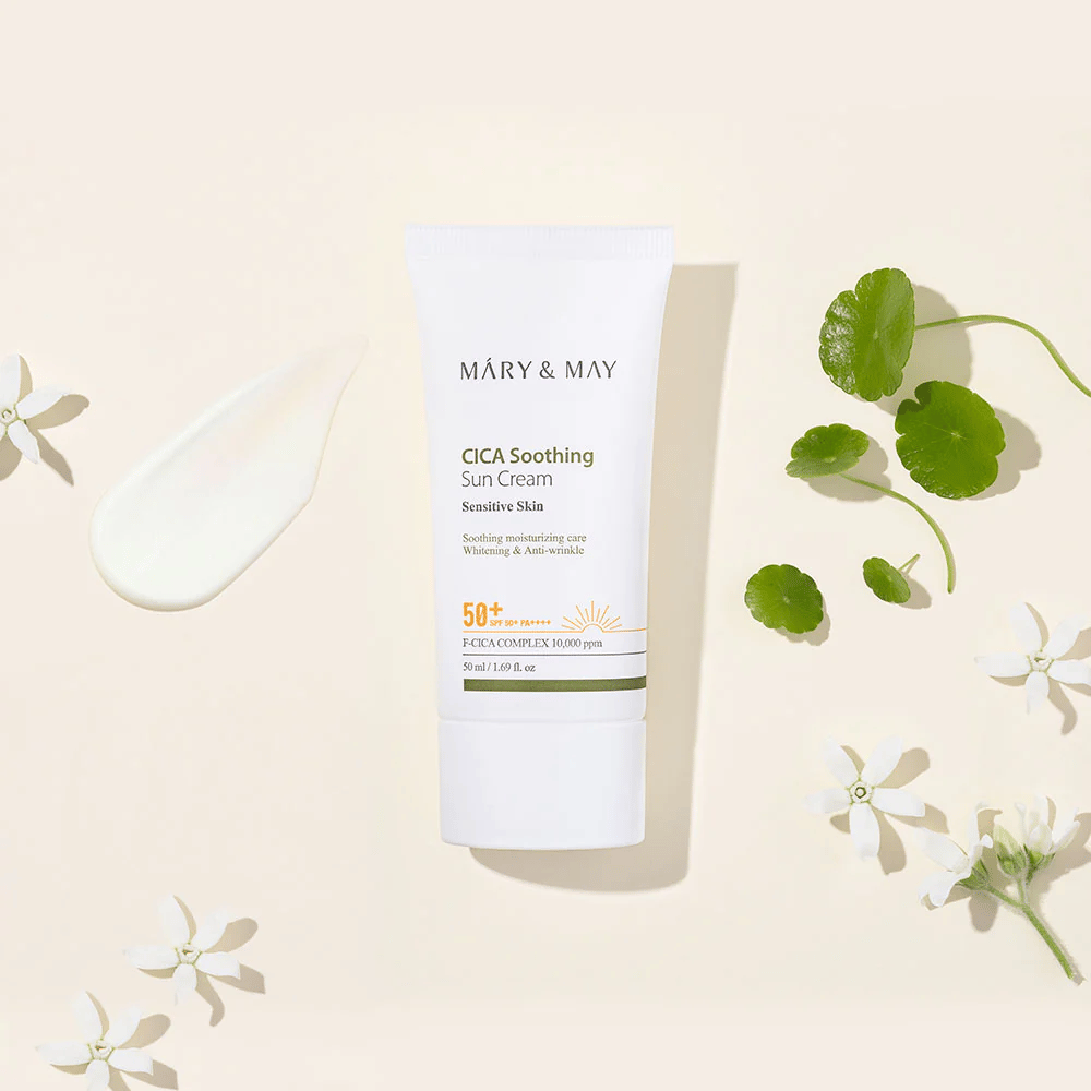 Mary&May CICA Soothing Sun Cream SPF50+ PA++++ presentada junto con una textura de crema, hojas de centella y flores blancas. La imagen destaca las propiedades calmantes del producto y su enfoque en la piel sensible.