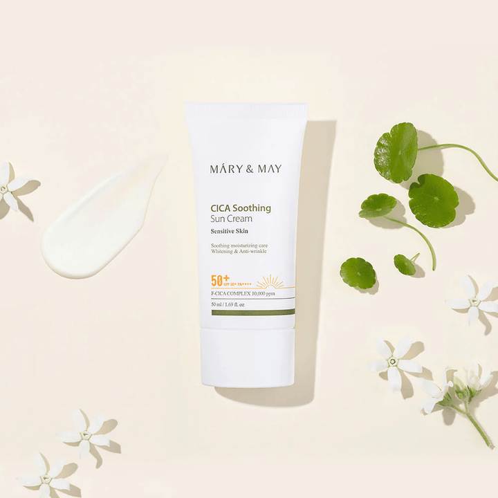 Mary&May CICA Soothing Sun Cream SPF50+ PA++++ presentada junto con una textura de crema, hojas de centella y flores blancas. La imagen destaca las propiedades calmantes del producto y su enfoque en la piel sensible.