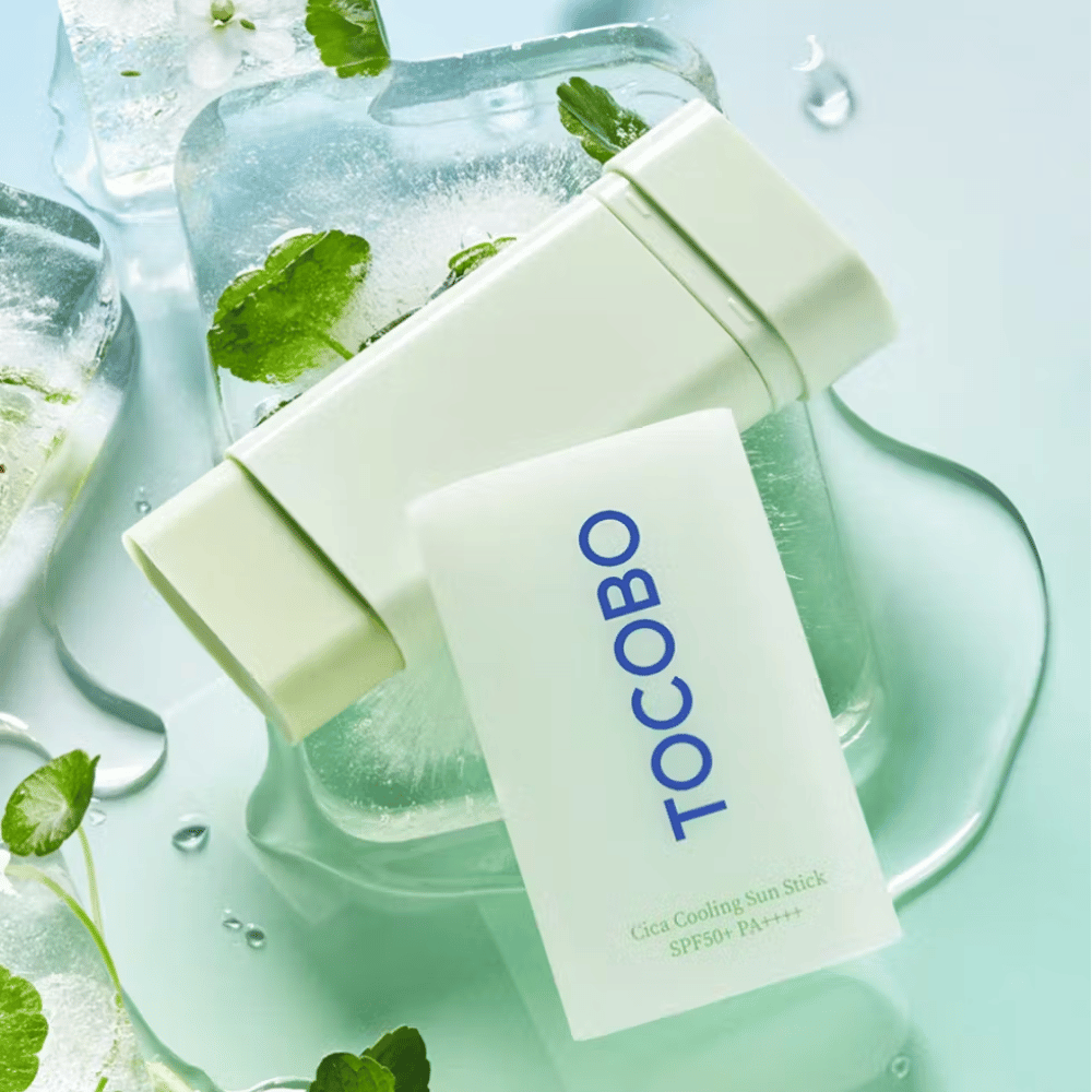 Tocobo Cica Cooling Sun Stick SPF50+ PA++++ sobre cubitos de hielo con hojas de plantas verdes, transmitiendo una sensación refrescante y vigorizante.