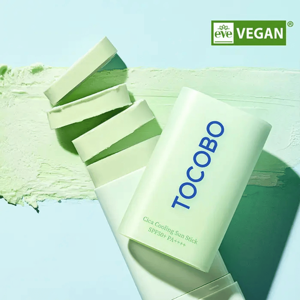 Tocobo Cica Cooling Sun Stick SPF50+ PA++++ en un empaque verde claro con certificación vegana (EVE VEGAN), ubicado sobre una capa de protector solar en barra verde.