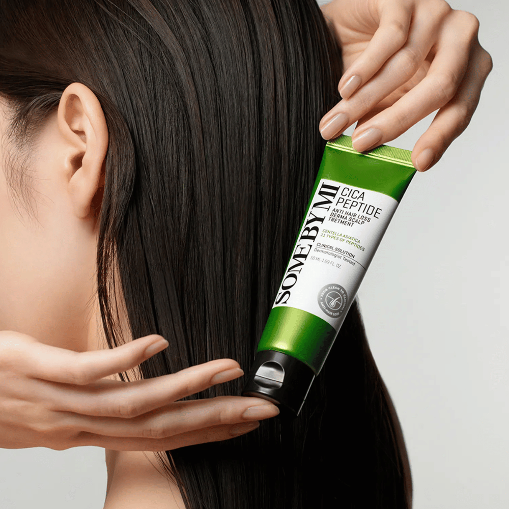 Mujer aplica SOME BY MI Cica Peptide Anti Hair Loss Derma Scalp Treatment en cabello largo y oscuro con un tubo verde y blanco.