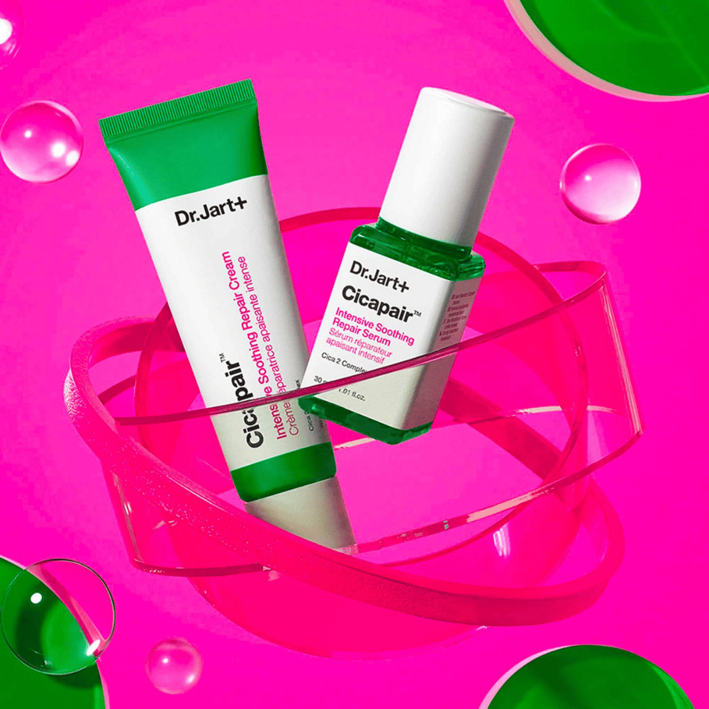 Dr.Jart+ Cicapair Intensive Soothing Repair Cream y Serum en envases verdes, que están sobre una base circular rosa. Los productos están diseñados para calmar y reparar la piel irritada.