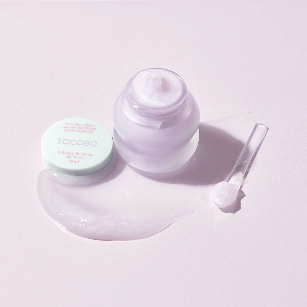 Frasco abierto TOCOBO Collagen Boosting Lip Mask con espátula y crema lila esparcida sobre fondo lila claro.